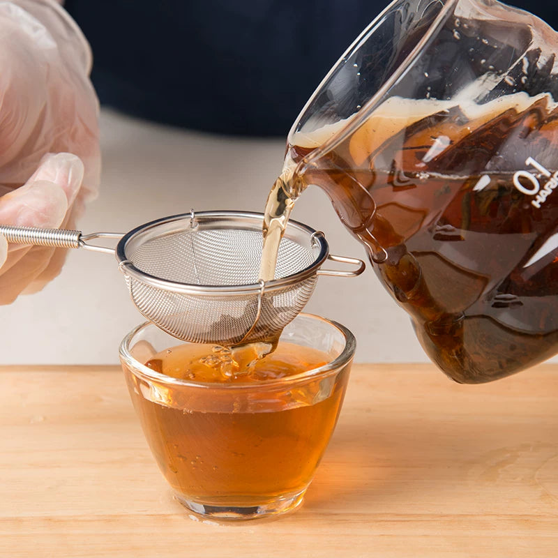 Pouring tea through a fine mesh stainless steel strainer into a glass cup