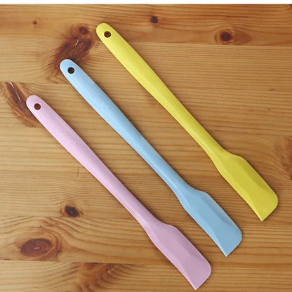 Pink, yellow and blue CakeLand small silicone spatulas on a wooden table