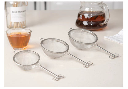 Small, medium and large stainless steel strainers beside a tea cup and teapot