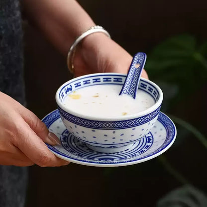 Hands holding a blue-and-white Linglong dessert bowl with matching plate and spoon